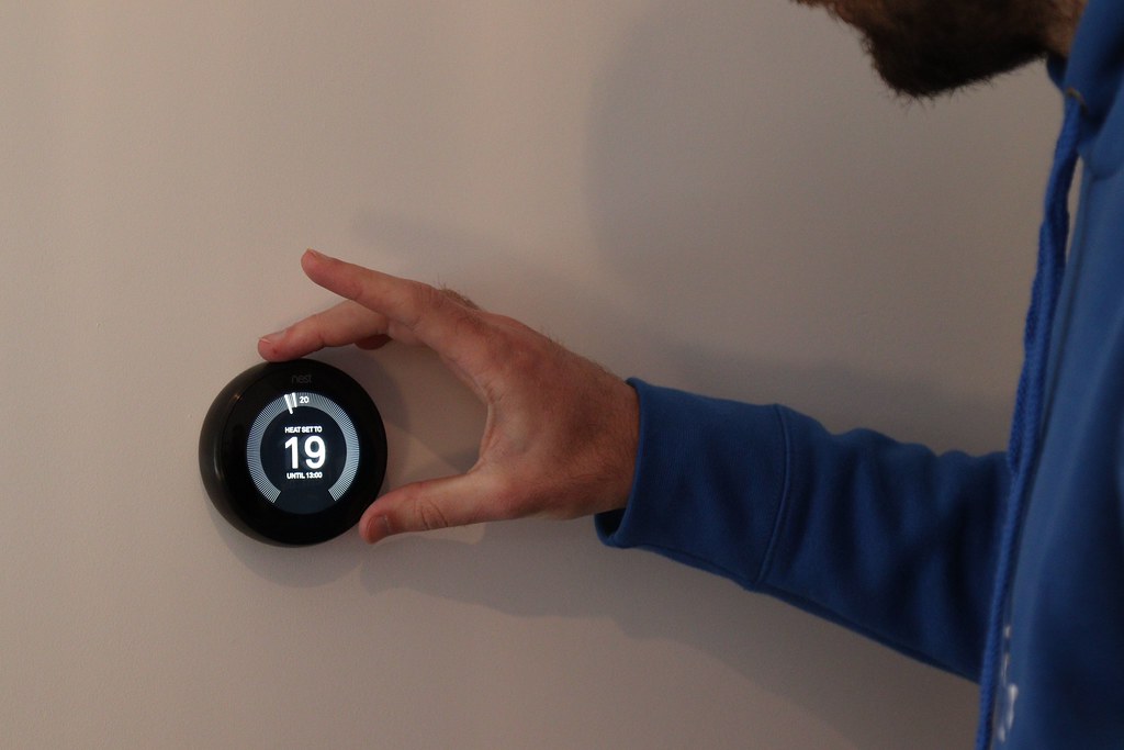A smart thermostat mounted on a wall displaying temperature (smart thermostat rebates)