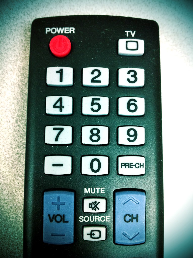A television remote control pointed at a screen showing streaming app icons