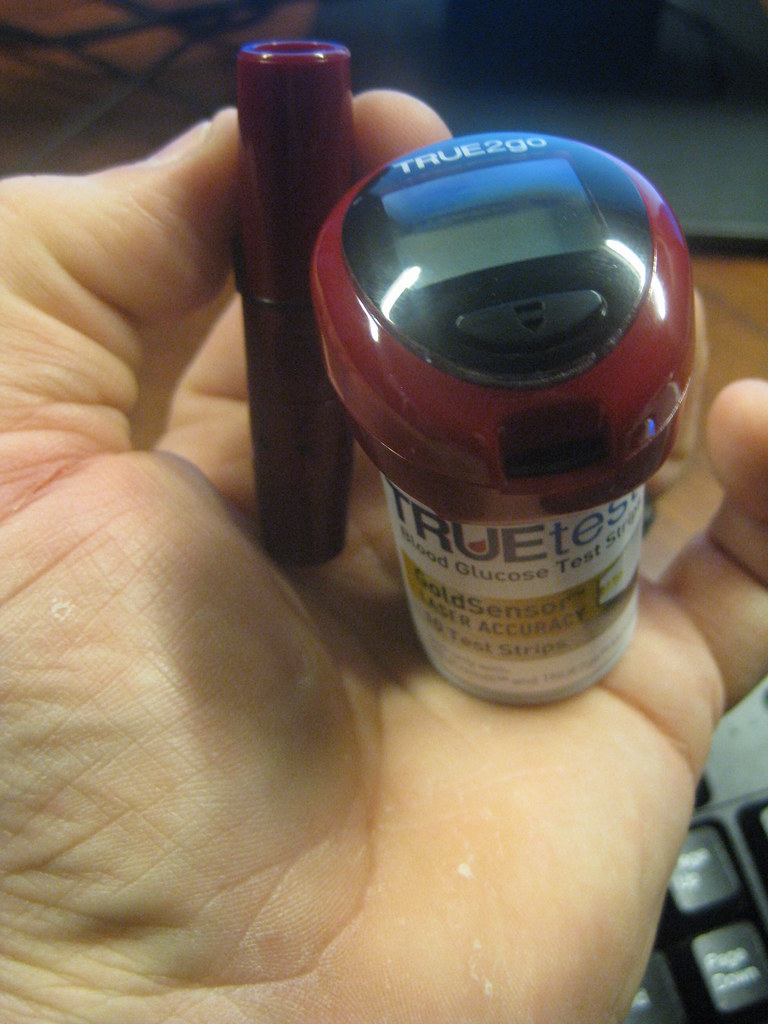 A continuous glucose monitor sensor attached to a person's arm, with a phone showing glucose data (cgm)
