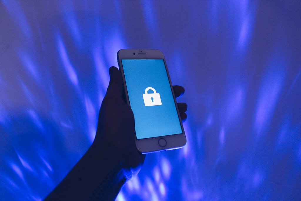 A hand holding a phone showing a padlock icon, representing data privacy (data broker opt out)