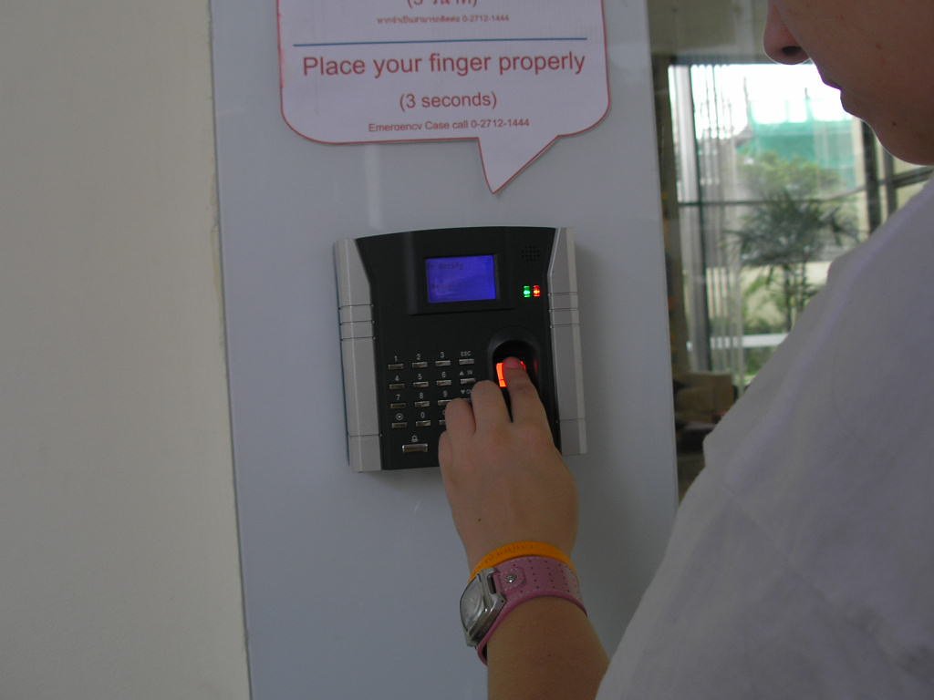 A person pressing a finger to a wall-mounted fingerprint scanner (passkeys)