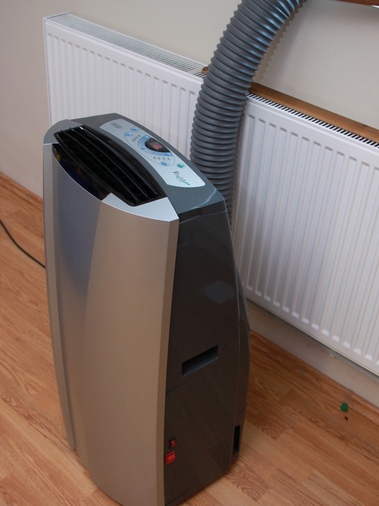 A portable air conditioner unit in a room with its exhaust hose vented through a window (portable ac unit)