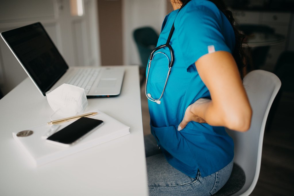 A person at a desk with a hand on their lower back (posture corrector)