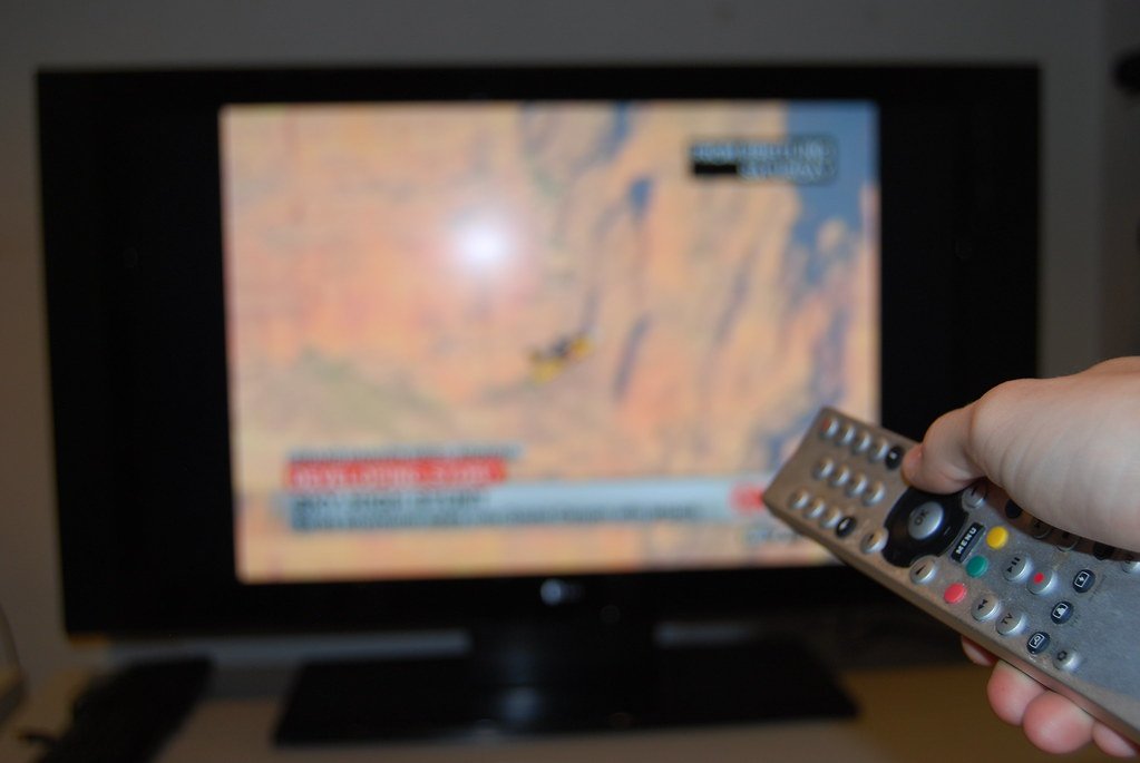 A hand holding a remote control in front of a television (acr tracking)