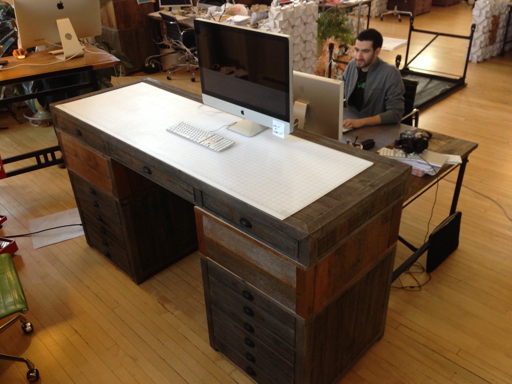 A standing desk converter raised on top of an office desk with a monitor and keyboard