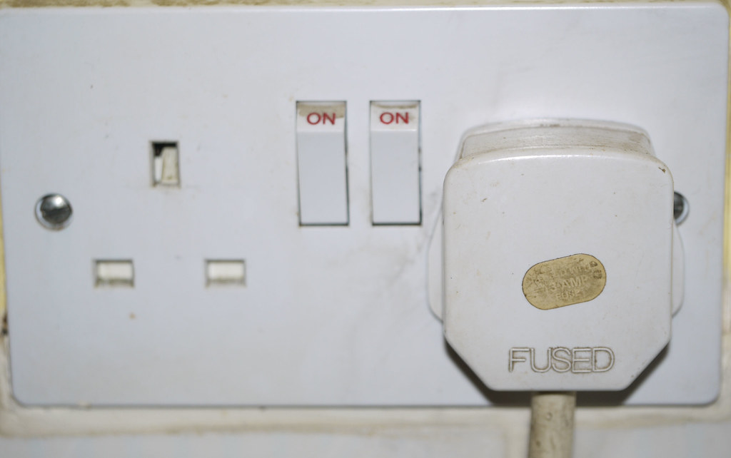 A universal travel plug adapter plugged into an international wall outlet (travel adapter)